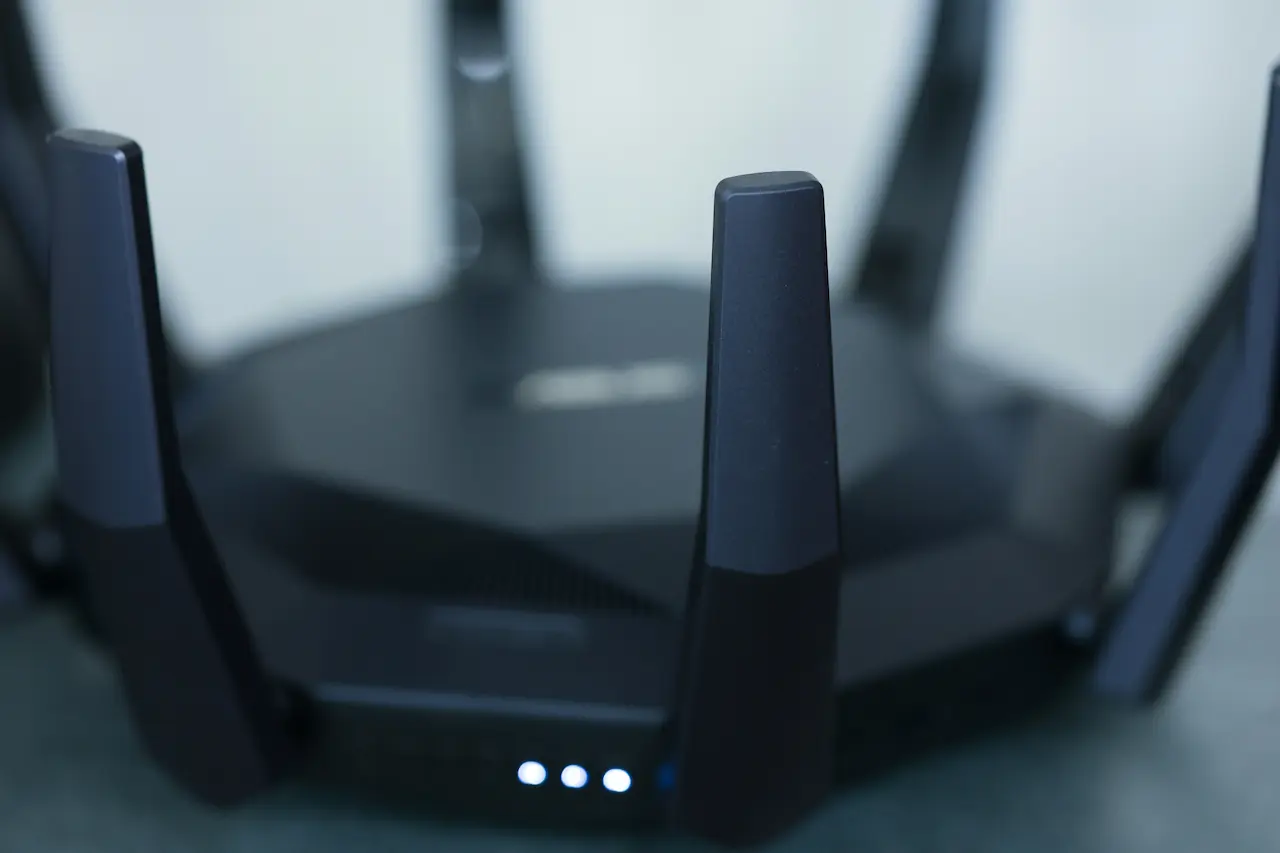 Nowoczesny router Wi-Fi z kilkoma antenami i świecącymi diodami LED, ustawiony na płaskiej powierzchni.